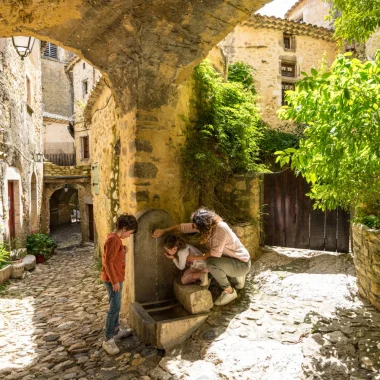 Family drinking at a fountain in the village of outstanding character of Saint-Montan, in spring