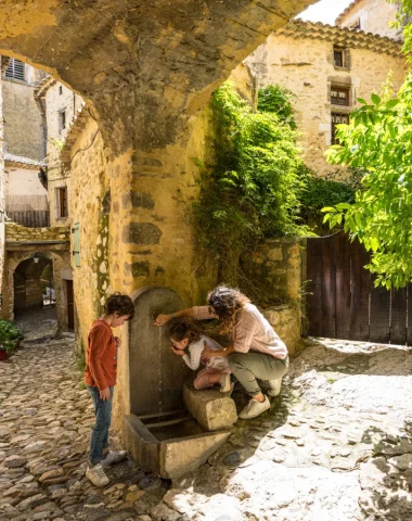 Family drinking at a fountain in the village of outstanding character of Saint-Montan, in spring