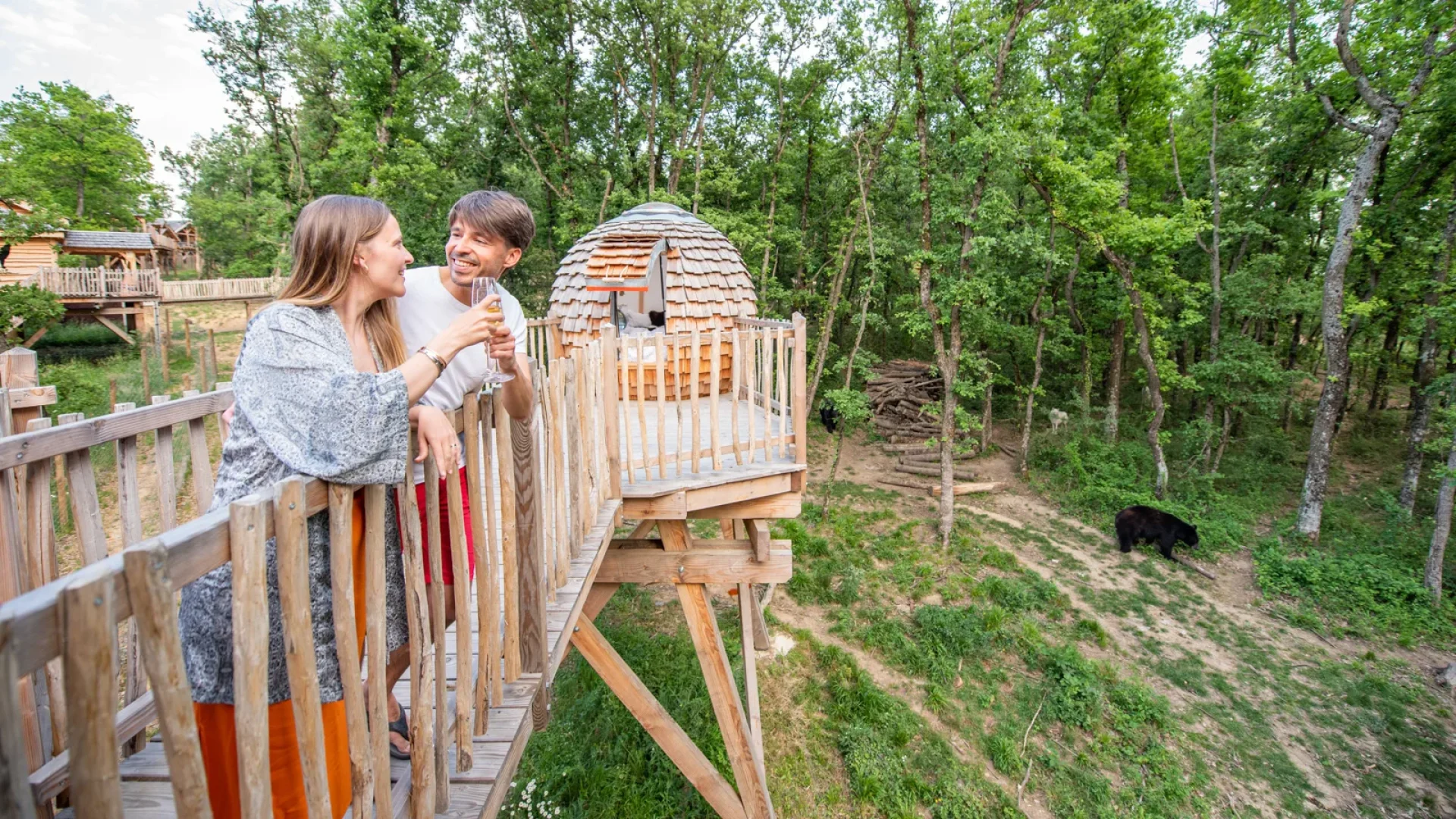 Couple toasting in an unusual accommodation: the “Perched Cabins” of the Peaugres Safari, above the wolves and bears
