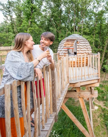 Couple toasting in an unusual accommodation: the “Perched Cabins” of the Peaugres Safari, above the wolves and bears